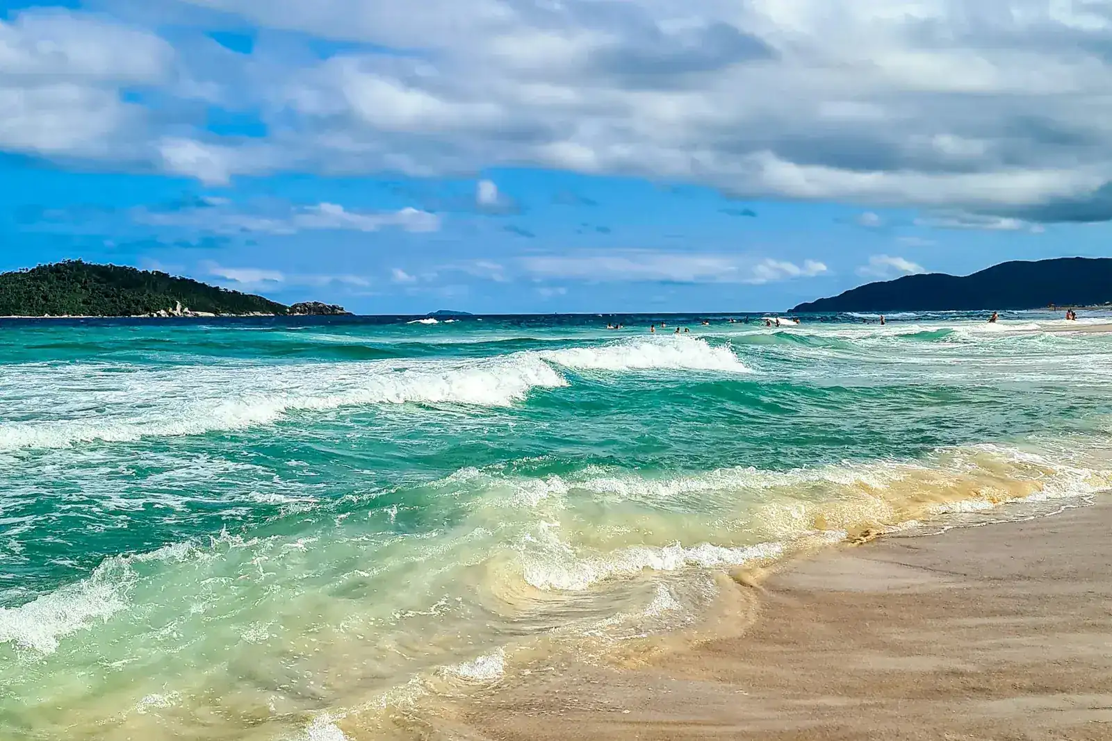 Olas turquesas llegando a la arena de la Playa de Campeche, con cielo azul y nubes blancas